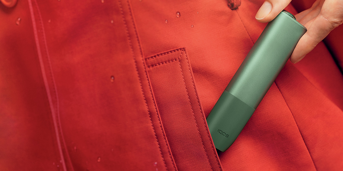 Dispositivo IQOS ILUMA ONE colore green dentro la tasca di un giacchetto rosso