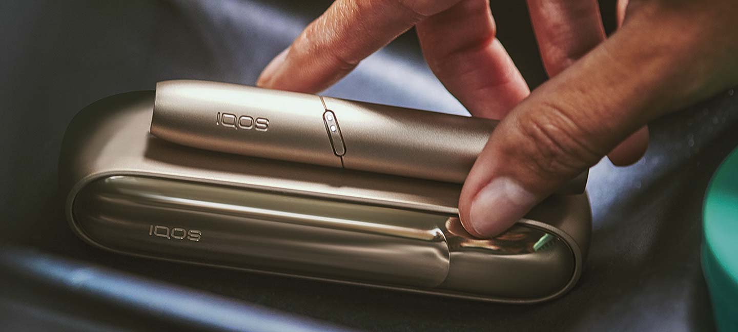 Una mano con un holder e un charger IQOS brilliant gold