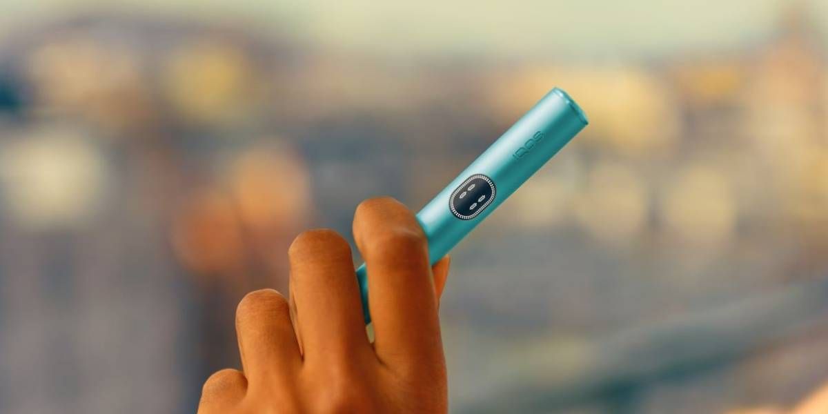 mano maschile che tiene holder IQOS ILUMA i colore breeze blue con touch screen accesso in nero