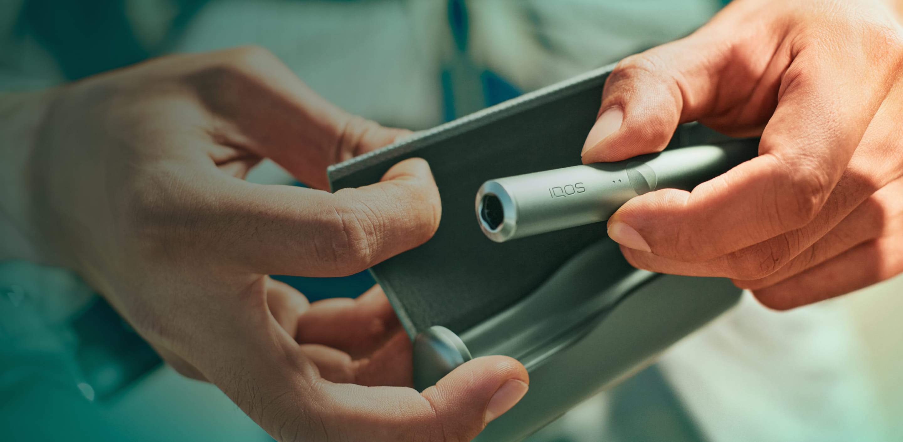 Hands opening an IQOS ILUMA Heated Tobacco device