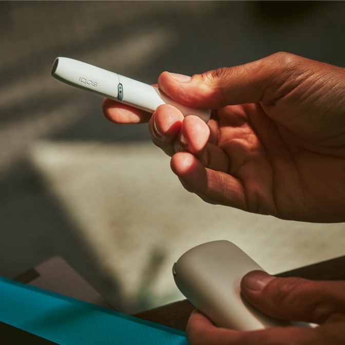 A woman with curly hair holding an IQOS device.
