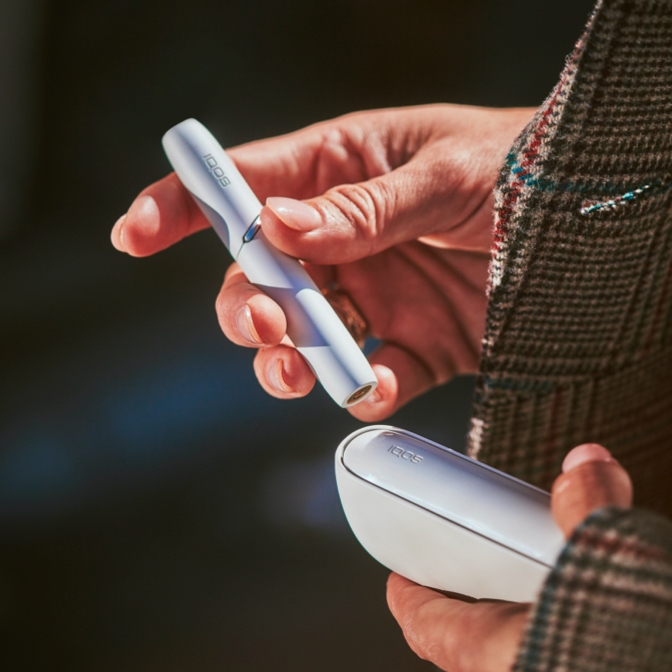 Una donna con in mano un holder bianco e un charger IQOS nell'altra mano