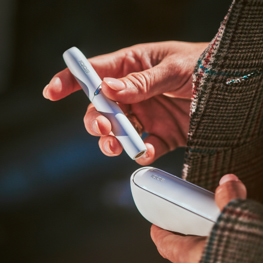A woman's hand with a white IQOS holder in one,  and charger in the other