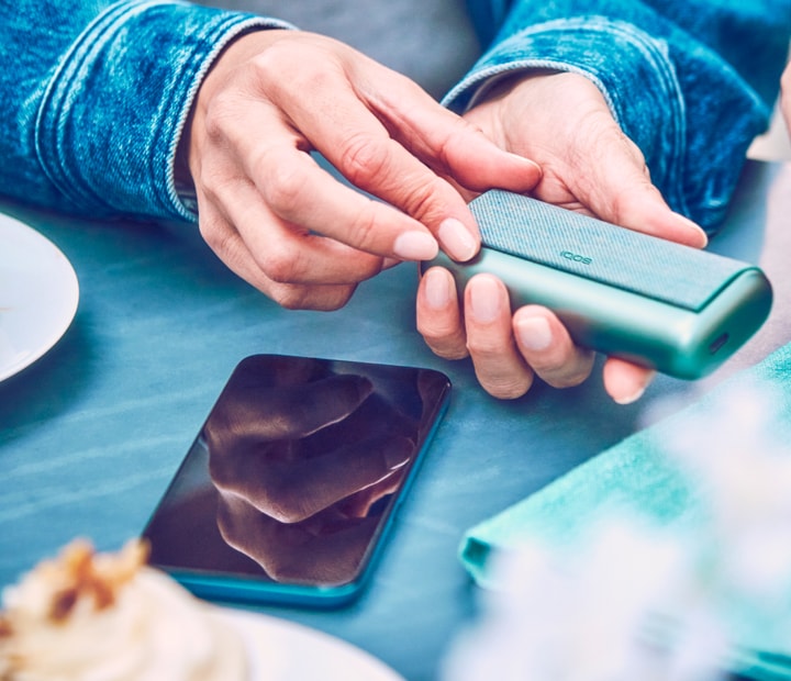 A person holding a Jade Green IQOS ILUMA PRIME Pocket Charger.