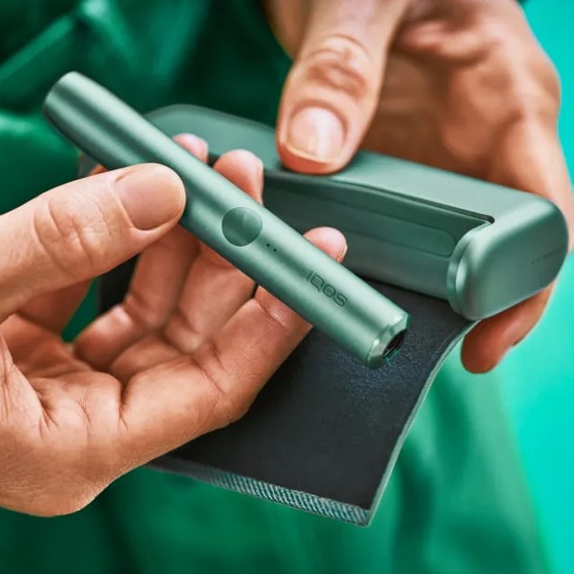 Man on a couch with his IQOS kit and the mobile in his hands