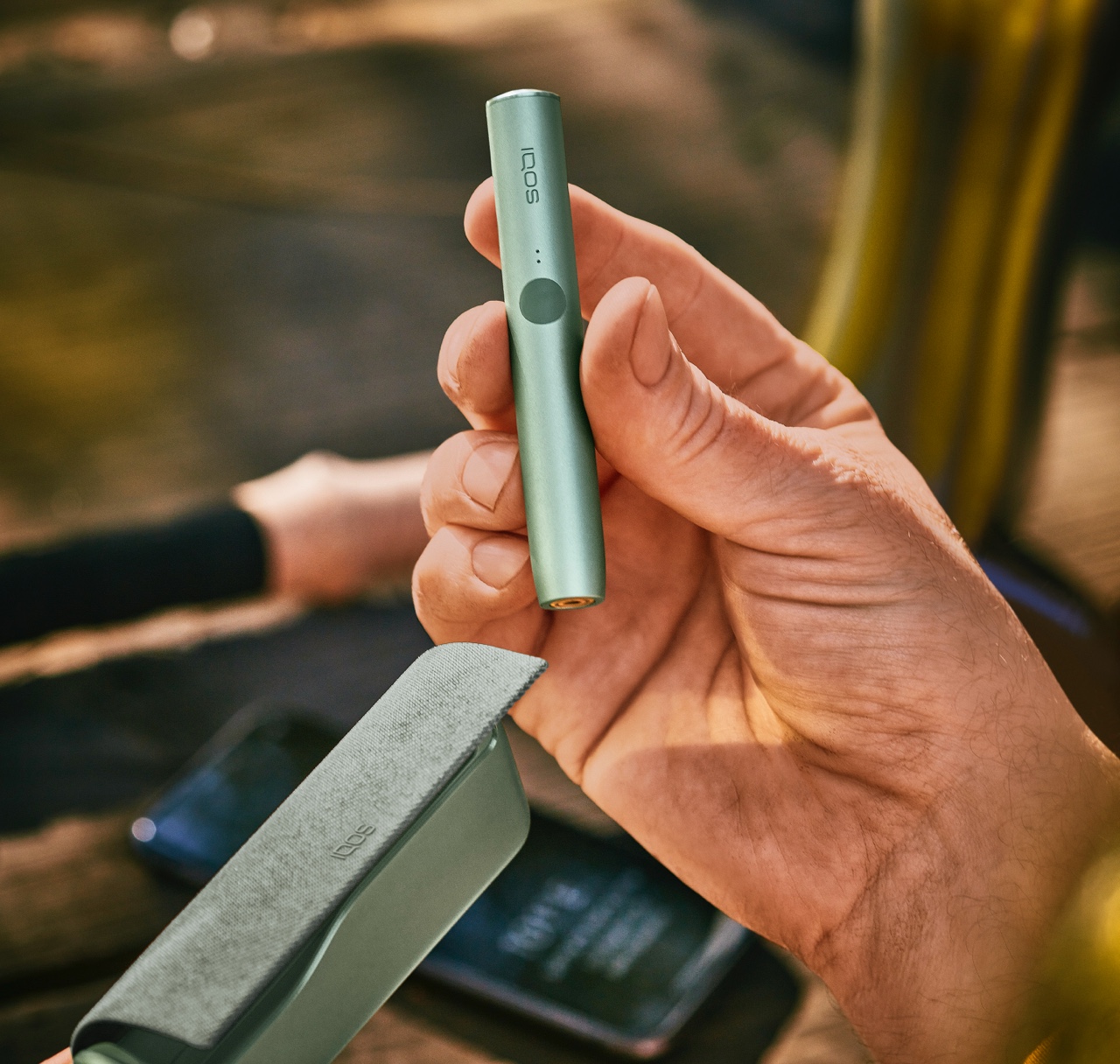 A moss green IQOS ILUMA Holder in a person's hand.