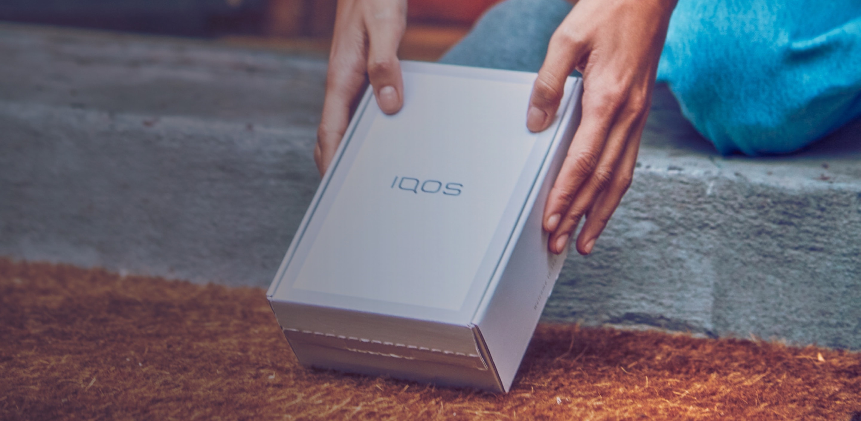 Two hands picking up a IQOS device box.