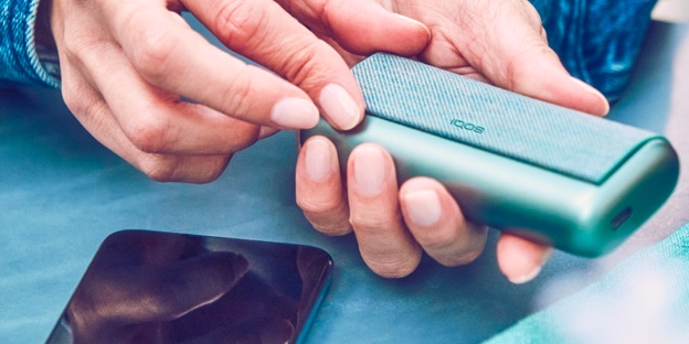 A woman holding an IQOS device looking at a laptop.