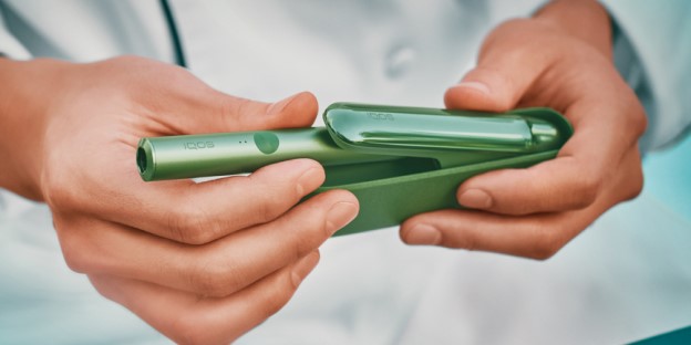 A woman holding an IQOS device looking at a laptop.