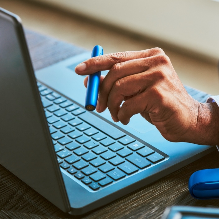 Stellar blue IQOS 3 DUO holder and charger in businessman's hand with HEETS stick inserted