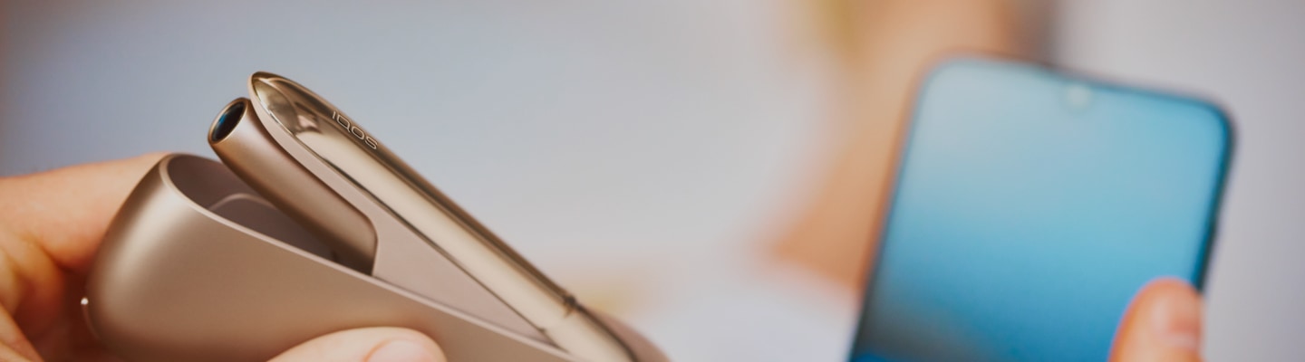 Person with a gold IQOS Duo and a blue mobile in his hands