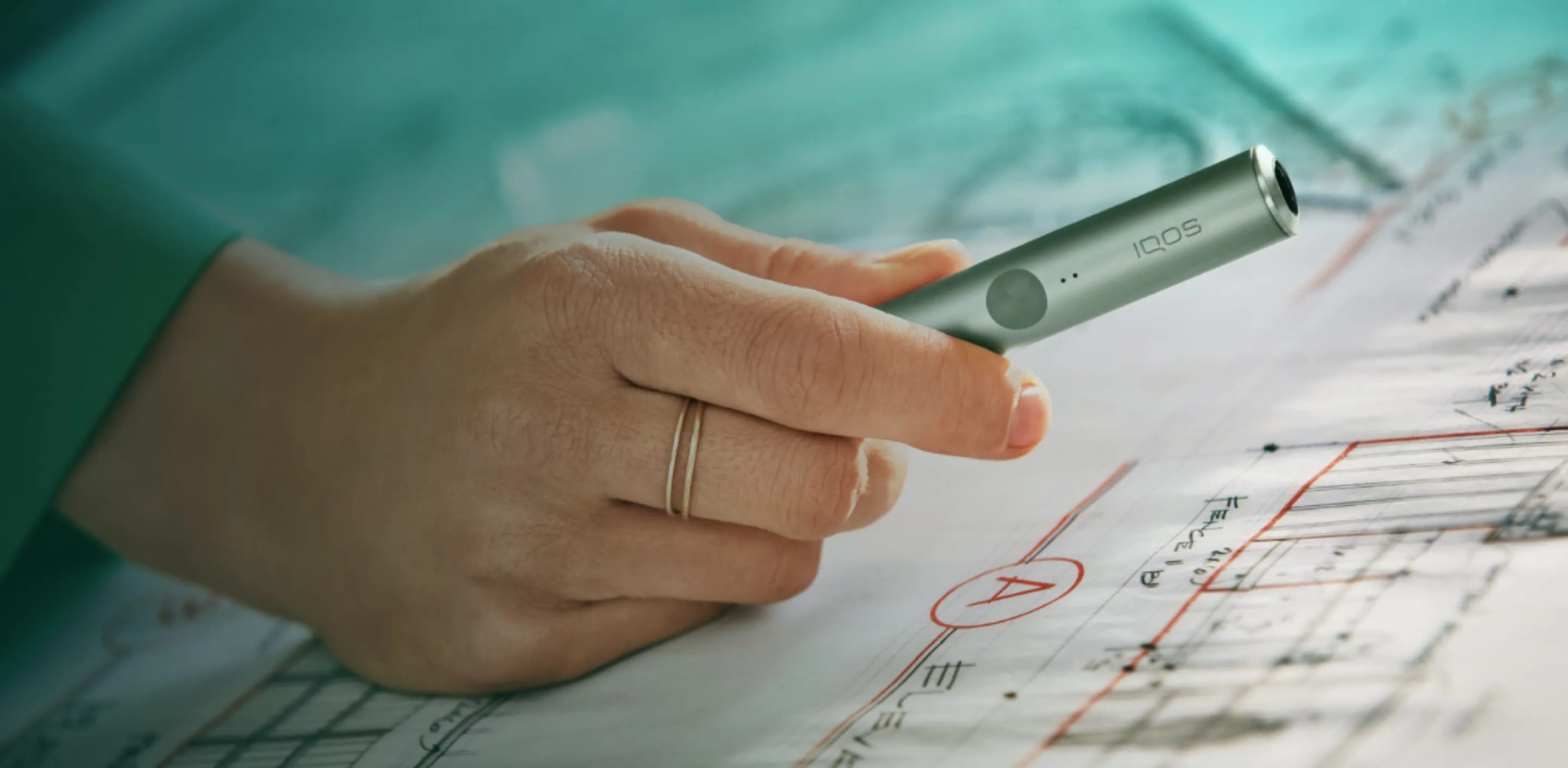 Un dispositivo IQOS sorretto da una persona e un cellulare sorretto da un'altra persona