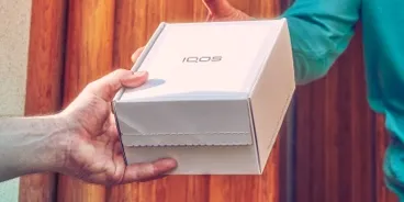 Una persona che consegna una scatola di dispositivi IQOS a una donna sorridente.