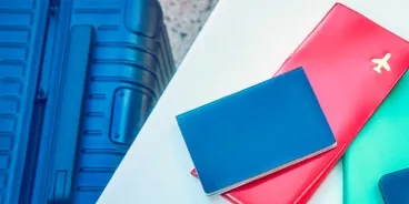 Una donna seduta a un tavolo accanto alla sua valigia con smartphone, passaporto e biglietto aereo.
