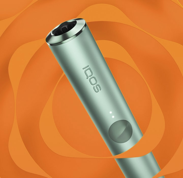 Holder of IQOS ILUMA in green color depicted obliquely and placed over an orange background with icon of SMARTCORE INDUCTION SYSTEM, induction system of iqos iluma line forming a kind of stylized rose