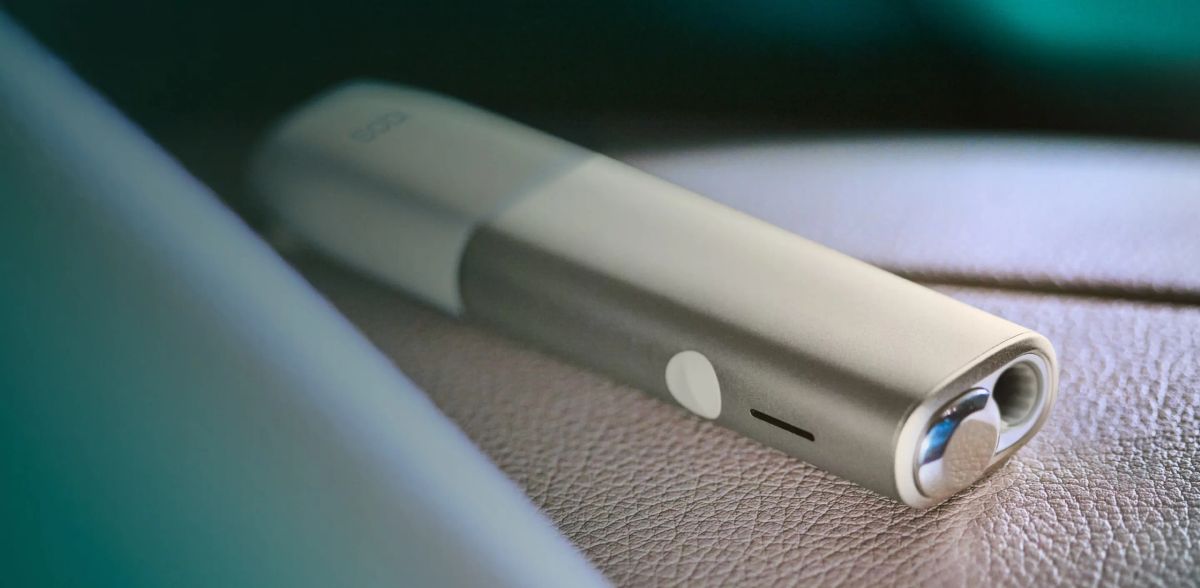Dispositivo iqos iluma one di colore grigio su una texture in pelle.