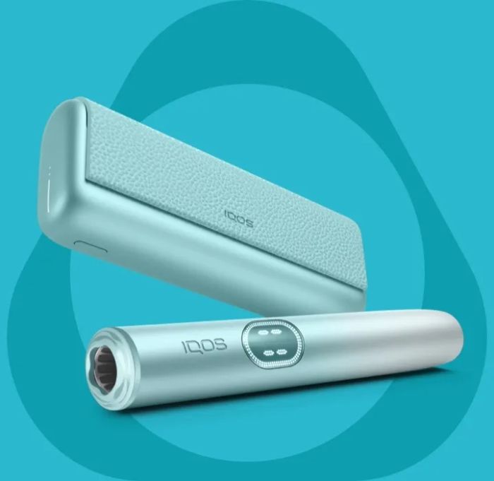 IQOS ILUMA i PRIME device colour turquoise Breeze Blue with pocket loader in oblique and holder outside loader resting horizontally. All on a turquoise background with the IQOS logo in grey.