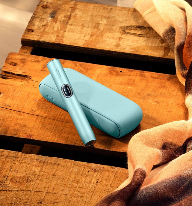 Turquoise IQOS device with its holder on a rustic wooden surface