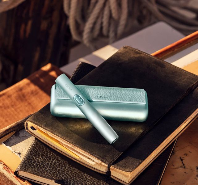 Turquoise IQOS device placed on books with soft lighting