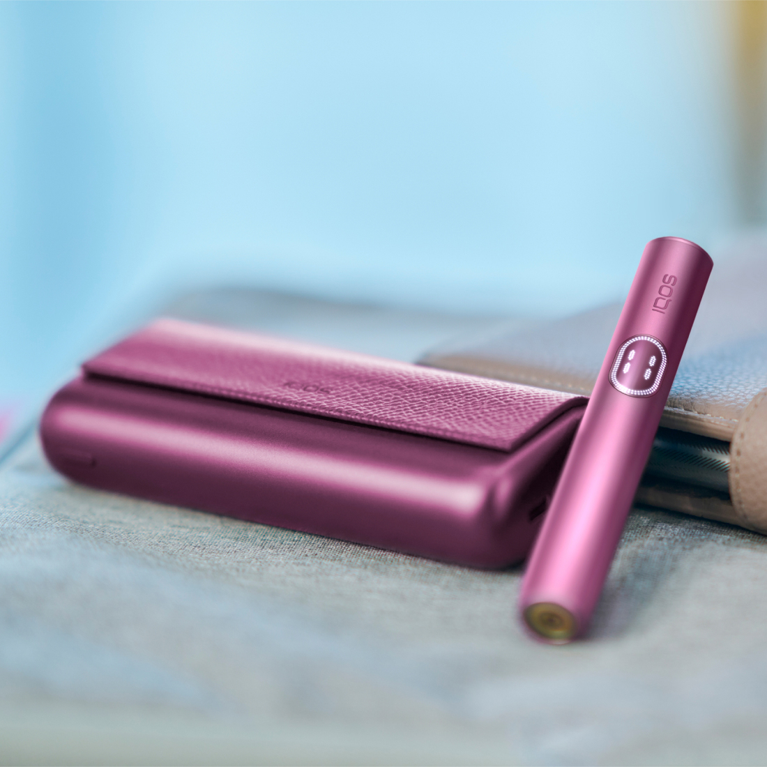 IQOS ILUMA i PRIME nel colore Garnet Red con holder e caricatore poggiato su un tavolo grigio