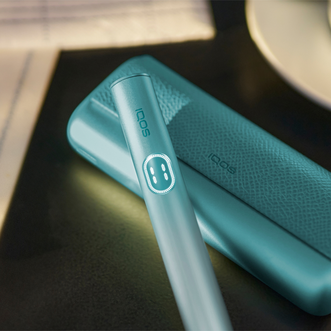 IQOS ILUMA i PRIME nel colore blu con holder e caricatore tascabile su un tavolo verde