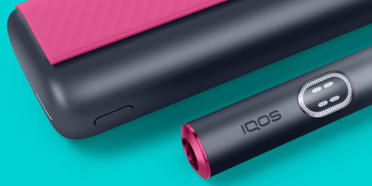 Red and black IQOS ILUMA i PRIME device and its charger on a light turquoise background