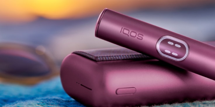 Garnet Red IQOS ILUMA i PRIME device and its charger on a blue fabric